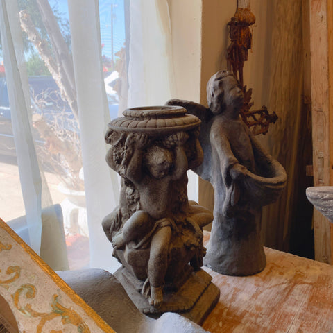 Three cherubs surrounding a candle stick made out of a dark grey stone. 